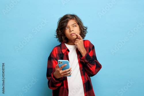 Young beautiful mixed race teenager, thought for a second, he holds a smartphone in his hand and looks away thoughtfully
