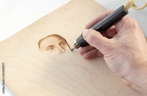 Photos Close-up drawing a portrait using hand burning wood with a pyrography pen, handm