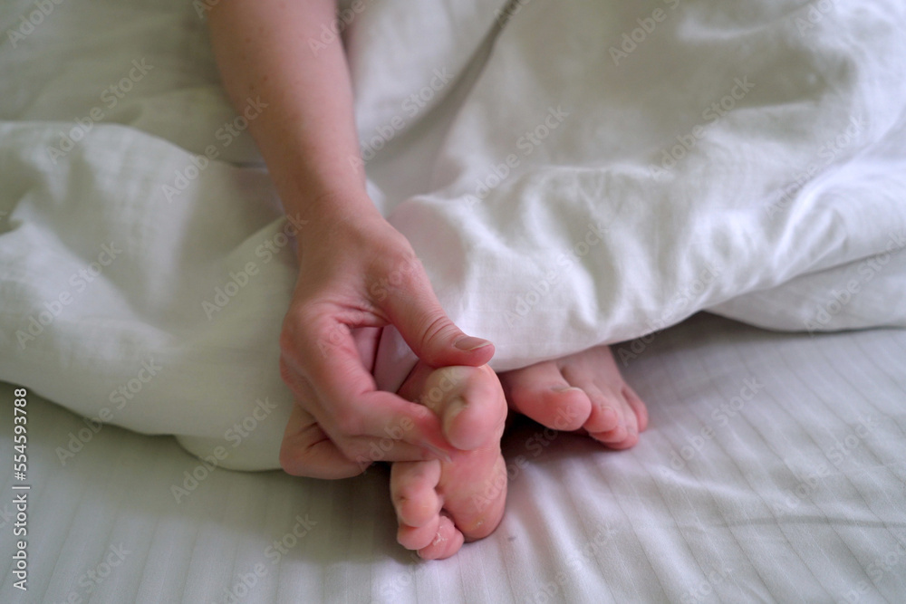 woman scratching her feet between her toes in bed, foot fungus disease woman scratching her feet between her toes in bed, foot fungus disease