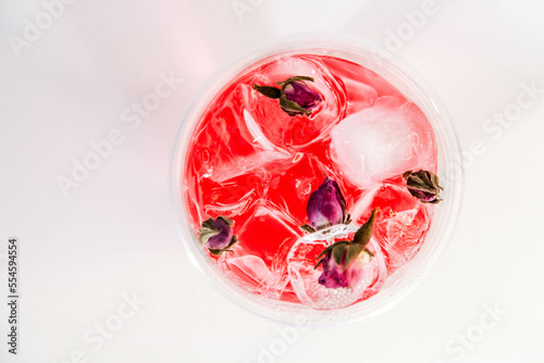 Pink lemonade with ice and pink rose buds in a transparent glass on a white background. View from above