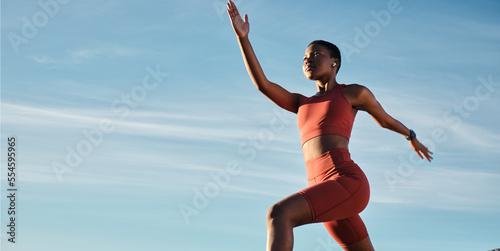 Black woman, music earphones or running in workout, training or exercise for healthcare, marathon or cardiovascular wellness. Low angle, sports or fitness runner on blue sky background with radio