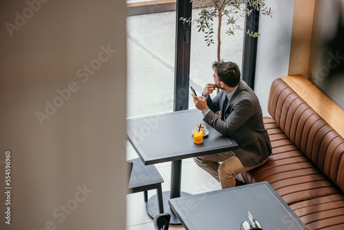 Pensive businessman in a gray suit  checking his emails on his mobile phone  drinking a coffee and fresh orange juice in the local cafe.