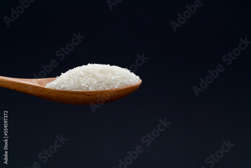 Wooden spoon with sugar crystals on black background