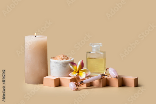 Burning candle, Natural massage oil, frangipani flower and sea salt scrab on beige background for wellness centre or spa cocnept. Modern presentation with geometric form photo