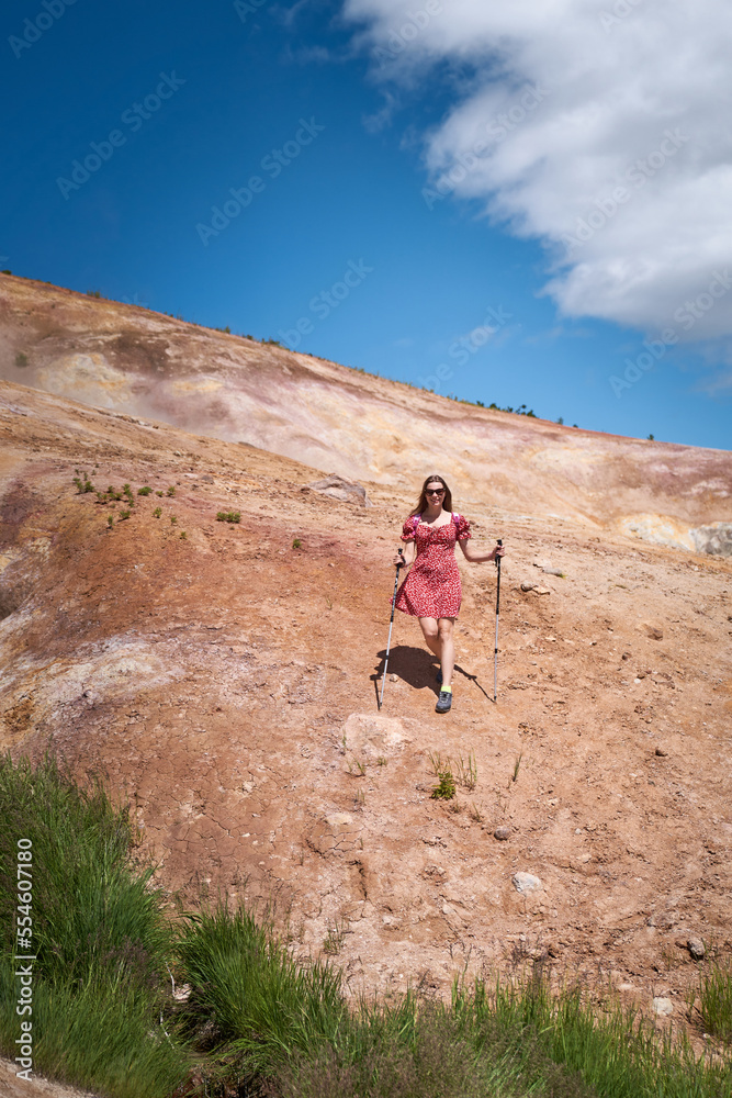 Young woman in a red dress hiking to the top of the mountain. Kamchatka peninsula
