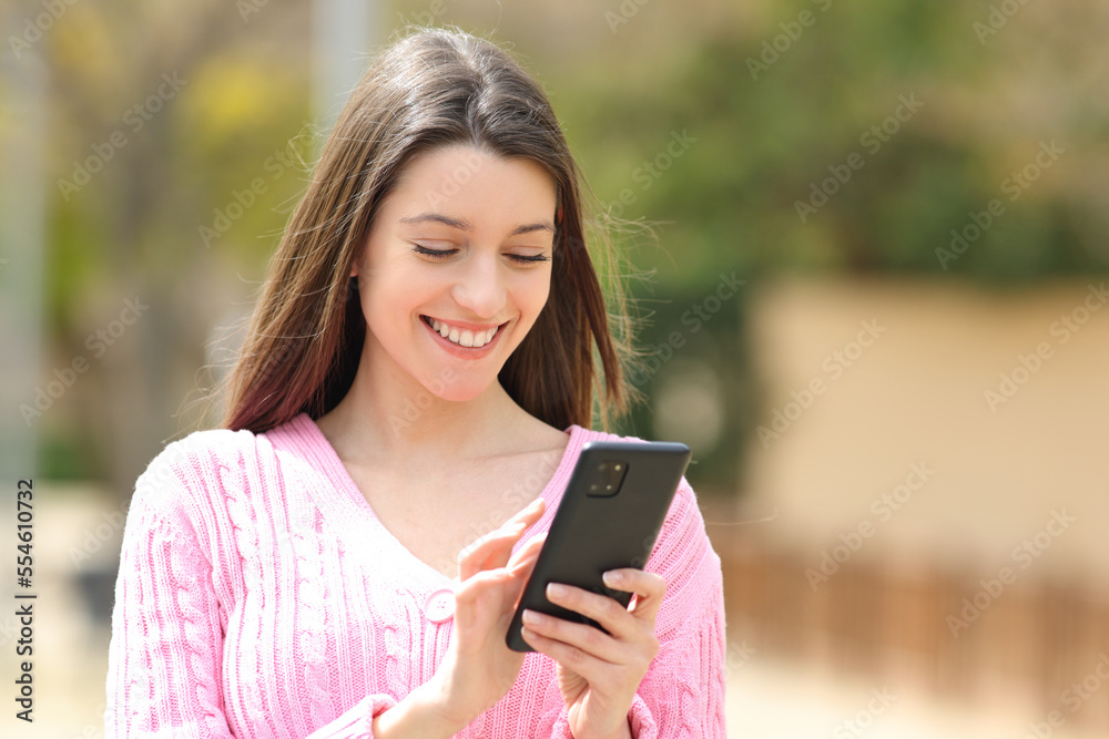 Happy teen in pink using phone in the street
