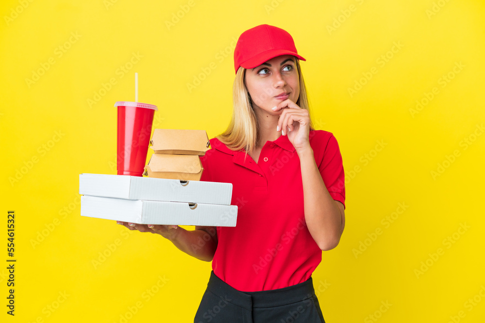 Delivery Uruguayan woman holding fast food isolated on yellow background looking up while smiling Delivery Uruguayan woman holding fast food isolated on yellow background looking up while smiling