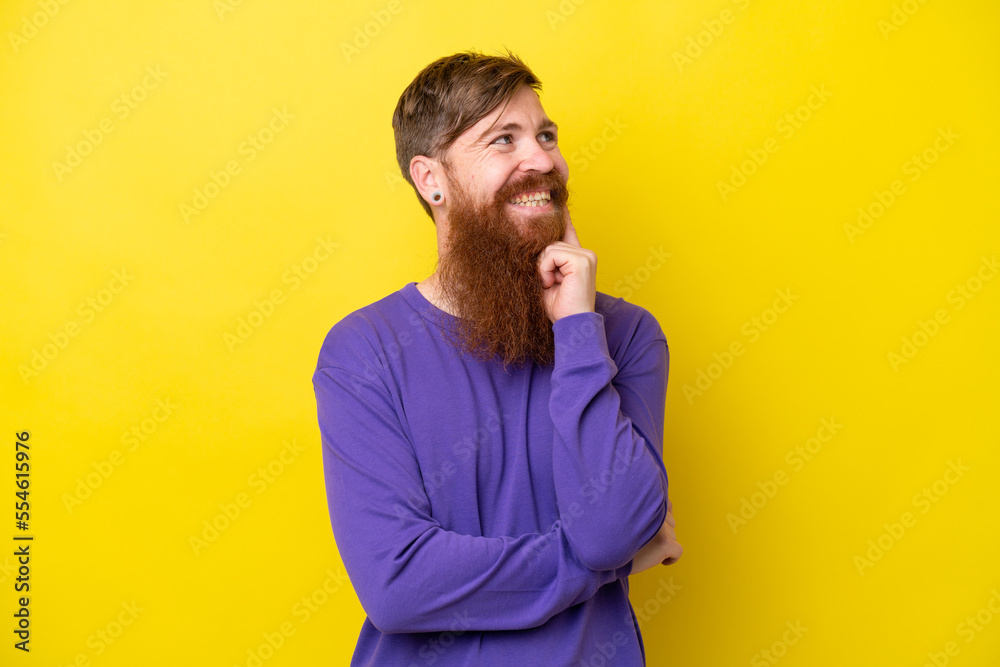 Redhead man with beard isolated on yellow background thinking an idea while looking up Redhead man with beard isolated on yellow background thinking an idea while looking up