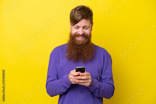 Redhead man with beard isolated on yellow background sending a message with the mobile