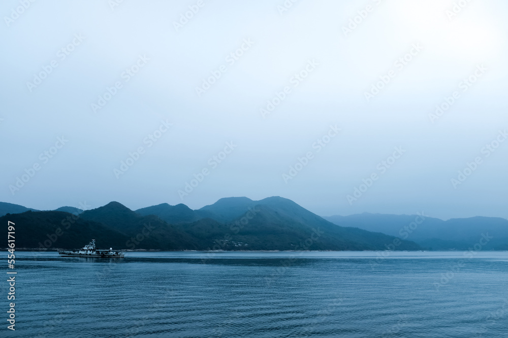 A boat on the calm sea with mountains as the background under cloudy weather