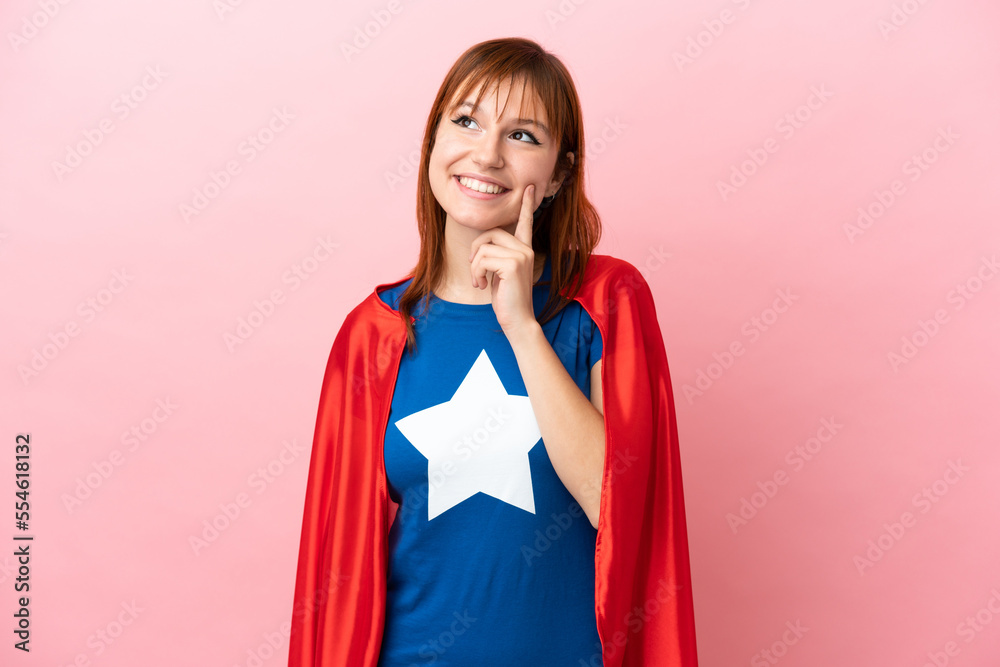 Super Hero redhead girl isolated on pink background thinking an idea while looking up Super Hero redhead girl isolated on pink background thinking an idea while looking up