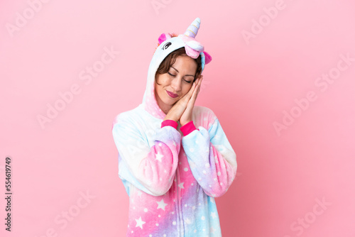 Young caucasian woman with unicorn pajamas isolated on pink background making sleep gesture in dorable expression