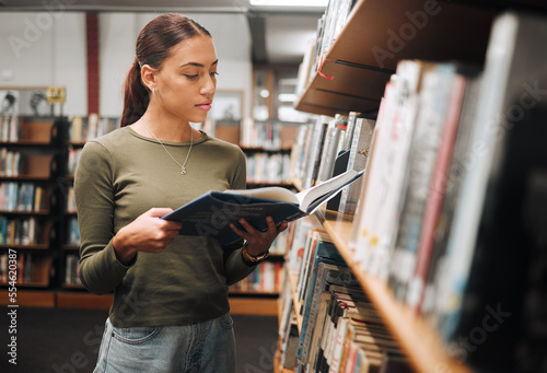 Black woman reading book in a library for education, studying and research in school, university or college campus. Focus, book and student at bookshelf for language learning or philosophy knowledge photo