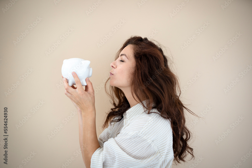 beautiful young woman with long hair posing in front of brown background with white piggy bank beautiful young woman with long hair posing in front of brown background with white piggy bank