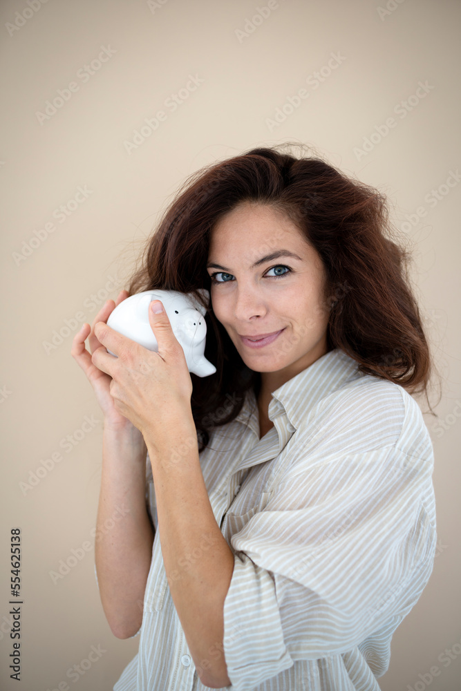 beautiful young woman with long hair posing in front of brown background with white piggy bank beautiful young woman with long hair posing in front of brown background with white piggy bank