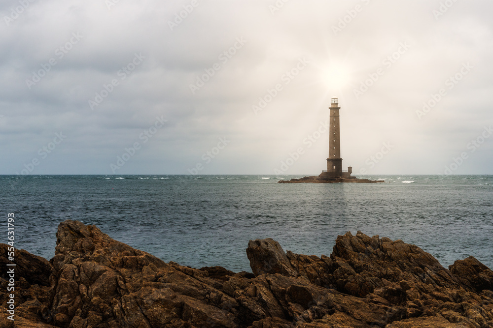 Fototapeta premium A scenic view of a lighthouse built on water near the shore with the sun shining brightly on top of it