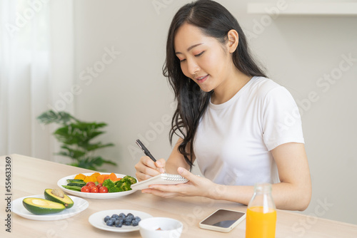 Diet  Dieting asian young woman write diet plan right nutrition on table with fresh vegetables salad  almond is different food ingredients in green. Nutritionist of healthy  nutrition of weight loss.