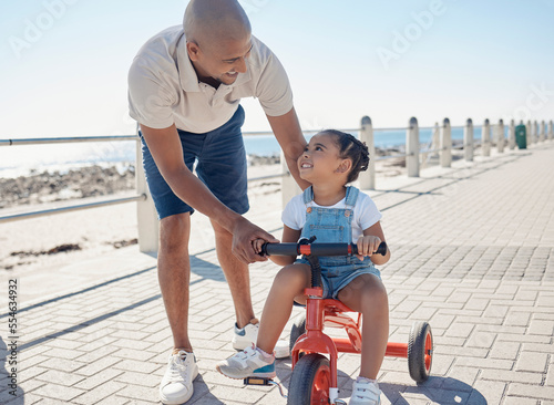 Father, girl child and tricycle at park, learning and happy in ocean sunshine on family vacation. Dad, daughter and happiness by sea promenade, teaching and smile on seaside holiday in San Francisco photo