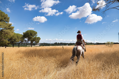 Woman horsewoman, young and beautiful, walking with her horse, in the countryside surrounded by dry grass. Concept horse riding, animals, dressage, horsewoman, cowgirl.