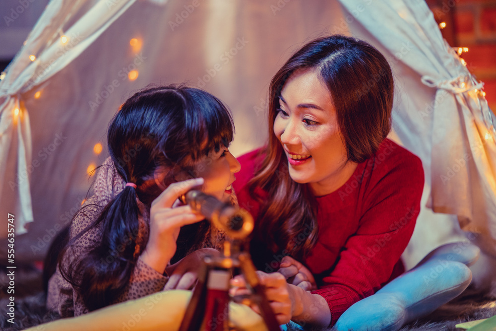 Happy mother and daughters in kids tent with telescope on Christmas eve. Celebrating Xmas at home.