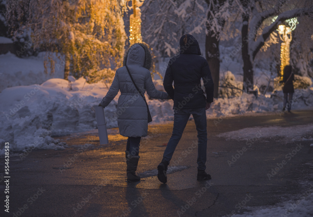 Young couple walking on snow at the Kalemegdan park in Belgrade.  View from the back. Winter scene at night.