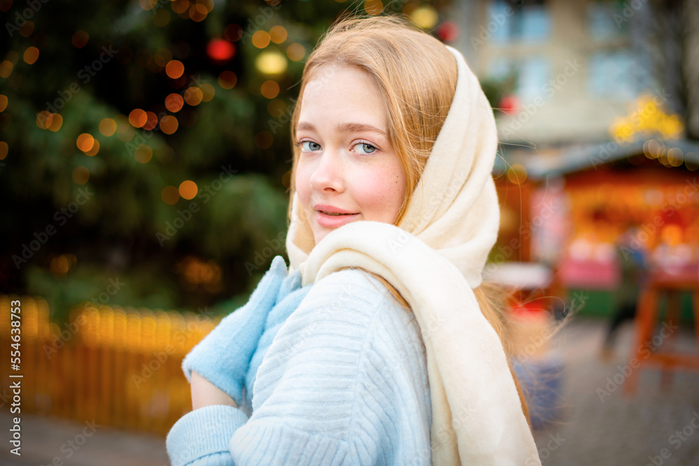 Portrait of A beautiful young girl walks around the festive Christmas city in a blue sweater and white scarf