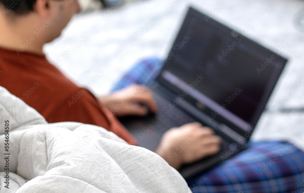 man in pajama working remote from laptop at home coding.programer sitting on floor carpet in kid baby room analyzing codes stats data.messy house thrown clothes.blurry man or laptop black screen 