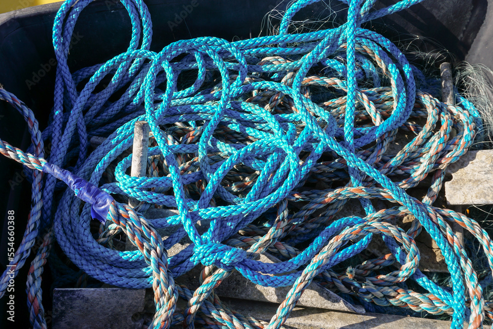 tangled sailing and fishing ropes by harbour. A messy pile of blue ropes.