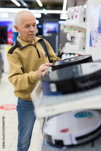 elderly man choosing robot vacuum cleaner in showroom of electrical appliance store