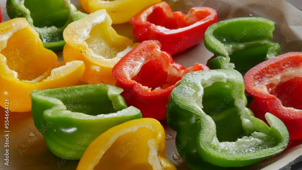 Halves of yellow, red, green paprika pepper with spices and sunflower oil lie on a baking sheet parchment before baking Halves of yellow, red, green paprika pepper with spices and sunflower oil lie on a baking sheet parchment before baking