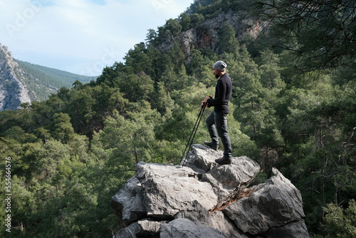 A hiker (Caucasian man) with trekking poles stand on the rock in the mountains on winter day. Goynuk gorge, Lycian way, Turkey.