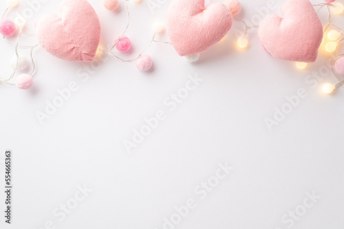 Saint Valentine's Day concept. Top view photo of fluffy heart shaped toys light bulb garland and soft pompons on isolated white background with empty space