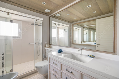 Luxurious bathroom with a large mirror with an unusual multiple reflection. Spacious shower area with glass railing. Daytime bright sunlight illuminates the huge bathroom  showing its splendor.