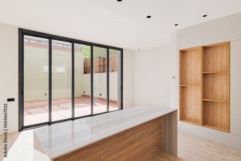 Fototapeta premium Empty interior of refurbished apartment with natural sunlight shining through big windows. Modern kitchen with island and wooden furniture.