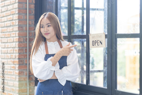 Portrait of happy waitress standing at restaurant entrance. Portrait of young business Asian woman attend new customers in her coffee shop. Smiling small business owner showing open sign in her shop. Free Download Portrait of happy waitress standing at restaurant entrance. Portrait of young business Asian woman attend new customers in her coffee shop. Smiling small business owner showing open sign in her shop. - GFXLoad