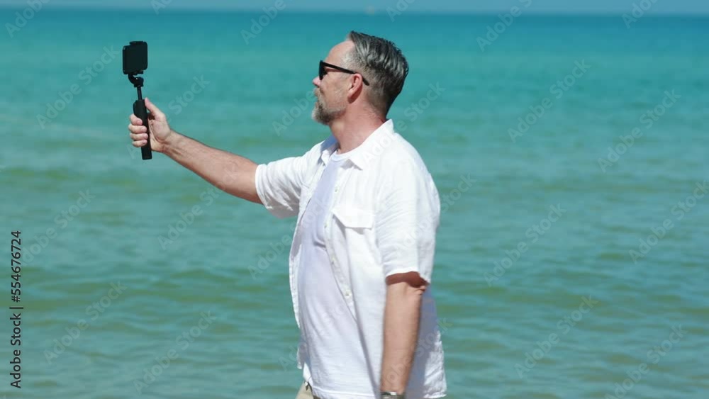 Senior caucasian male holding smart phone in hand shooting selfie photo on the beach. Vacation trip summer holiday. Senior caucasian male holding smart phone in hand shooting selfie photo on the beach. Vacation trip summer holiday.
