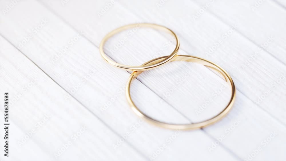 camera rotate around two gold wedding rings on a white wooden table.
