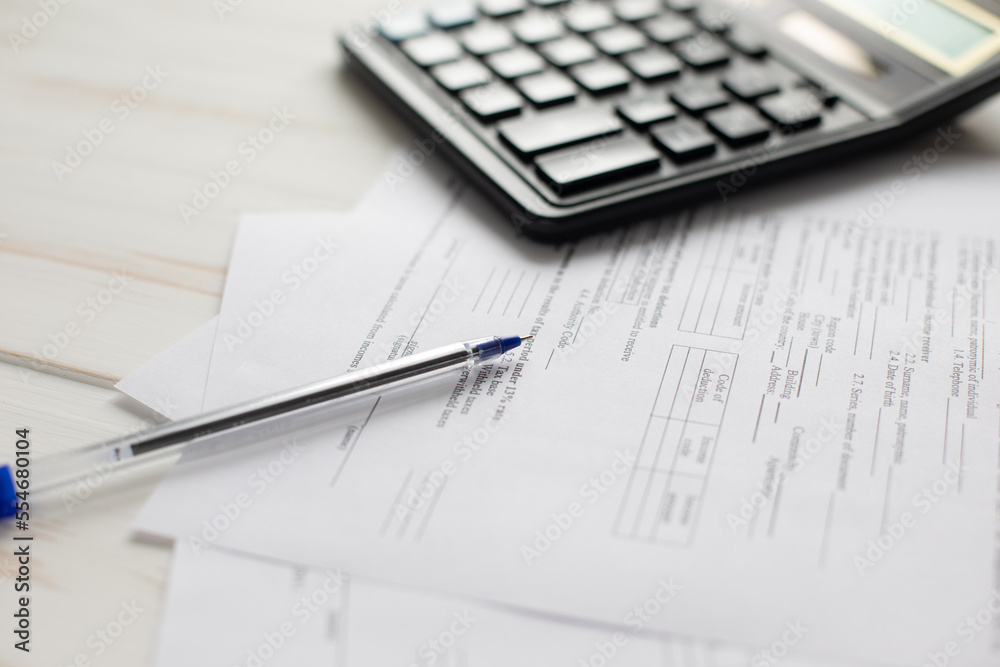 Photo of a pen lying on documents and a calculator in the background Photo of a pen lying on documents and a calculator in the background