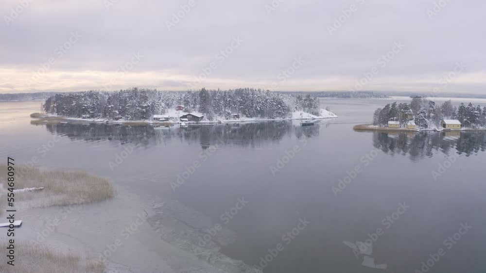 Soukka, Finland - 09.12.22: Top view of the snow-covered Islands with houses in Soukka. There is ice on the water in places. The boat is moving on the water. Winter landscape. Scandinavia. Soukka, Finland - 09.12.22: Top view of the snow-covered Islands with houses in Soukka. There is ice on the water in places. The boat is moving on the water. Winter landscape. Scandinavia.
