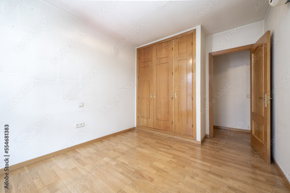 A built-in wardrobe with wooden doors and matching chests in a room with white walls and oak laminate flooring A built-in wardrobe with wooden doors and matching chests in a room with white walls and oak laminate flooring