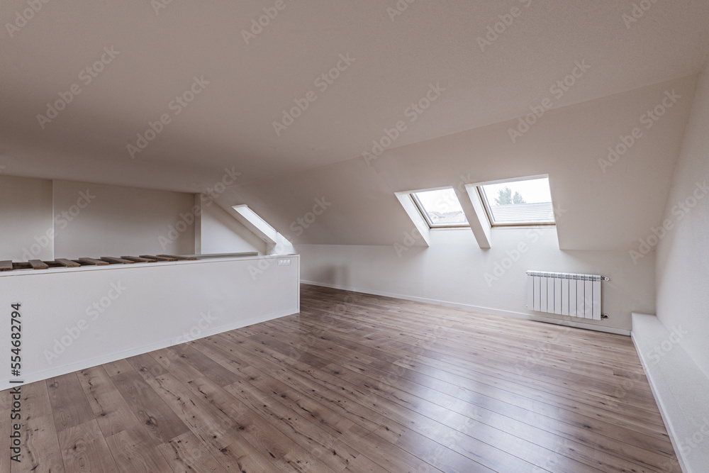 Attic of an empty single-family home with skylights on the eaves of the roof with chestnut floating flooring Attic of an empty single-family home with skylights on the eaves of the roof with chestnut floating flooring