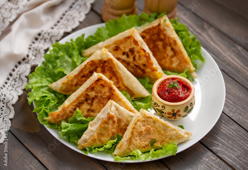 Mini Flatbread Wraps with cheese and ham filling. Fried patties from thin Armenian lavash served with tomato sauce on a white plate with lettuce leaves. Selective focus, horizontal, wooden table.