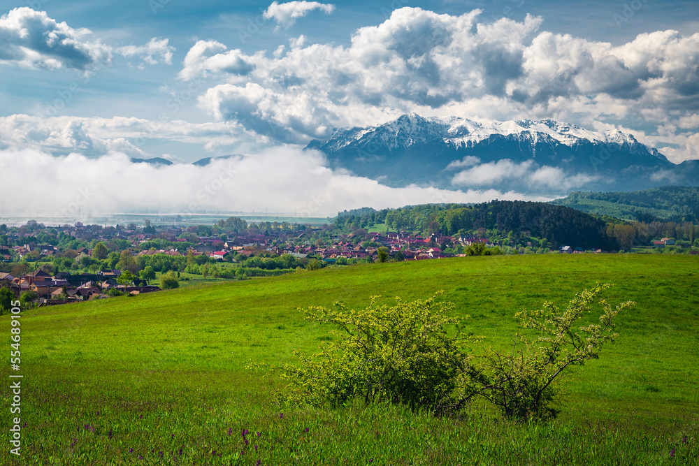 Misty spring landscape with green fields and snowy mountains, Romania Misty spring landscape with green fields and snowy mountains, Romania