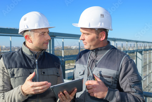 two men looking at tablet pc by perimeter fence