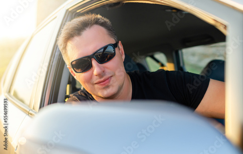 The man is driving a car. A handsome man in a black T-shirt drives a car at speed. © Denis Rozhnovsky