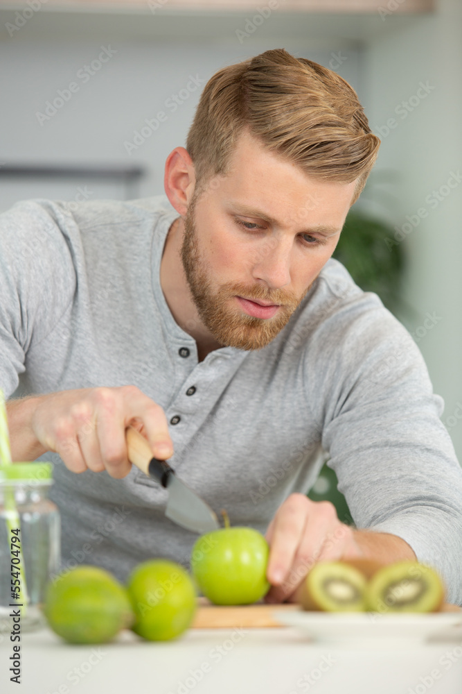 Fototapeta premium young man cutting fruit in the kitchen