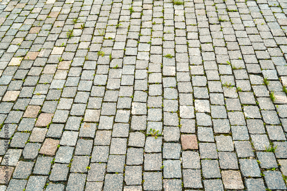 The texture of the stone pavement with grass between the stones close-up.