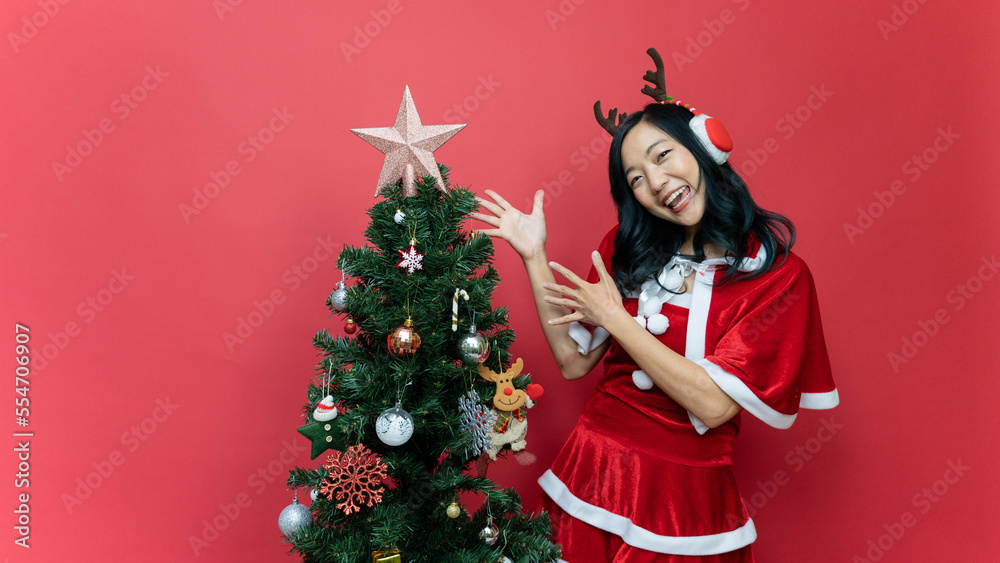 Happy beautiful young asian women in red santy costume have fun on Christmas holidays. The scene has a Christmas tree and a red background. Happy beautiful young asian women in red santy costume have fun on Christmas holidays. The scene has a Christmas tree and a red background.
