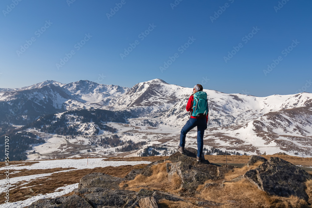 Rear view of woman with backpack looking at snow capped mountain peak Zirbitzkogel and Kreiskogel in Seetal Alps, Styria (Steiermark), Austria, Europe. Hiking trail Central Alps in winter on sunny day