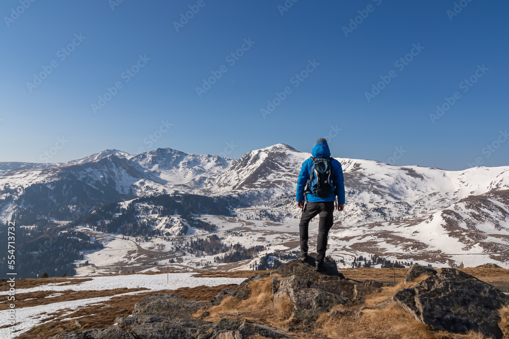 Rear view of man with backpack looking at snow capped mountain peak Zirbitzkogel and Kreiskogel in Seetal Alps, Styria (Steiermark), Austria, Europe. Hiking trail Central Alps in winter on sunny day